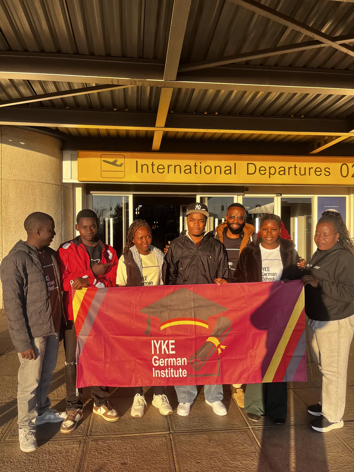 Iyke German Institute group at an international departure with the institute banner